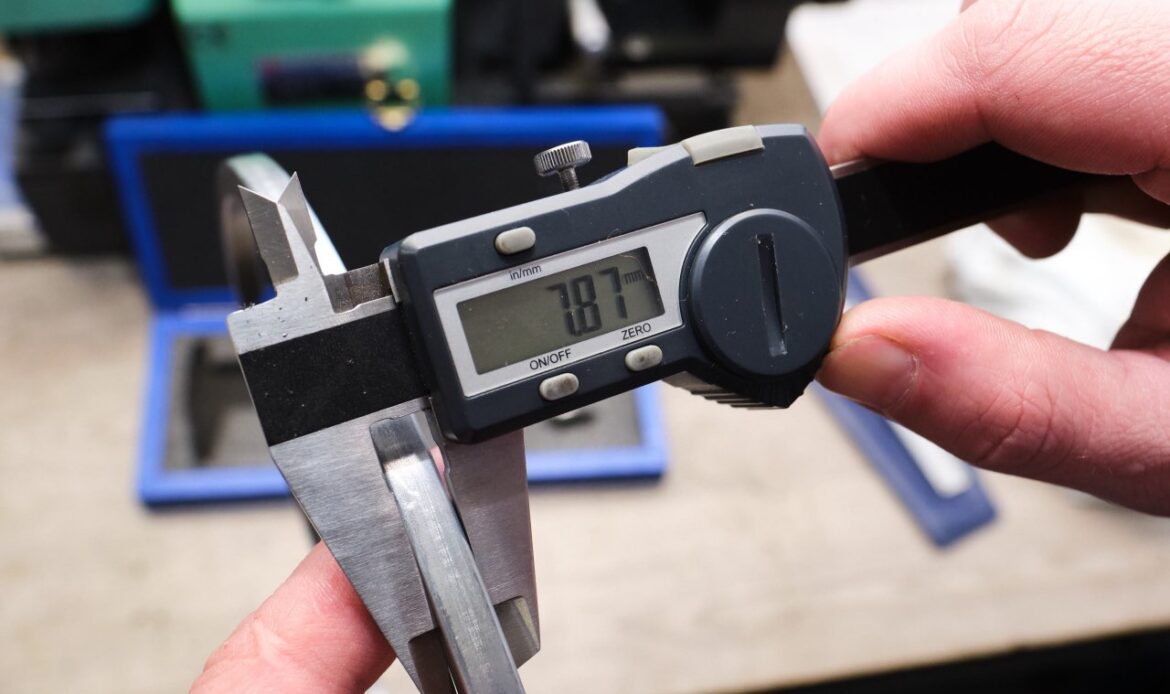 The process of measuring the thickness of a ring of a diesel engine using a caliper with a digital scale. In the background, manufacturing details in blur. Quality control